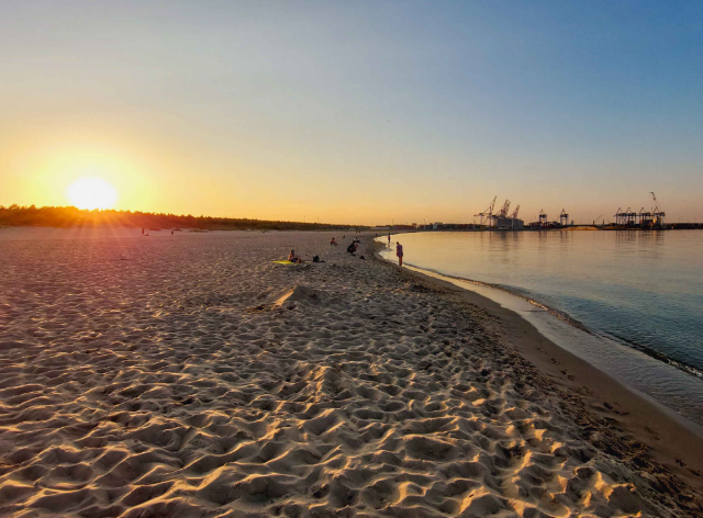 zachód słońca nad piaszczystą plażą i morzem, w tle konstrukcje przemysłowe