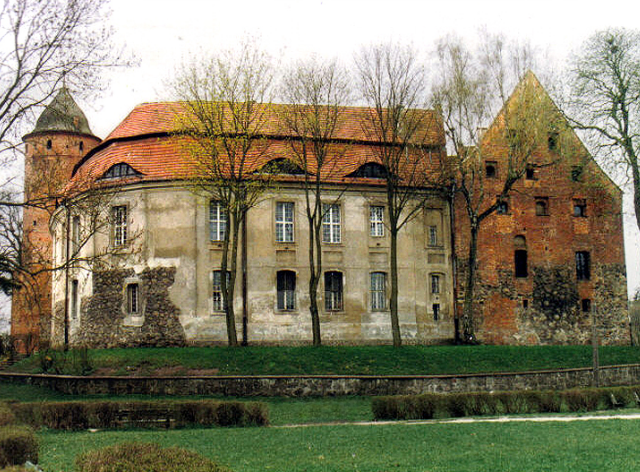 ceglany zamek z pozostałościami kamiennej konstrukcji, przed nim park