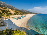 sandy coastline over transparent water, mountains in the background