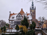 historic brick building with a sloping roof, tall church in the background