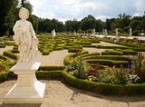 a statue of an angel on a pedestal, in the background a French garden