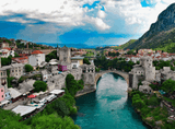 view of the city by the river with a stone bridge, mountains in the background