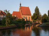 tall brick cathedral with a sloping red brick roof, river in the foreground
