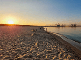 sunset over a sandy beach and the sea, industrial structures in the background