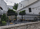 metal fence above a stone wall, buildings, vegetation, tables and chairs in the background