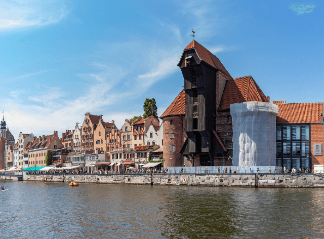 historic crane building by the water, with city buildings in the background